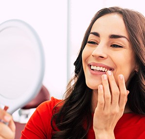 A woman using a hand mirror to admire her new dental implants