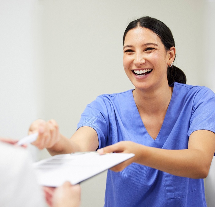 a dental assistant handing a patient forms